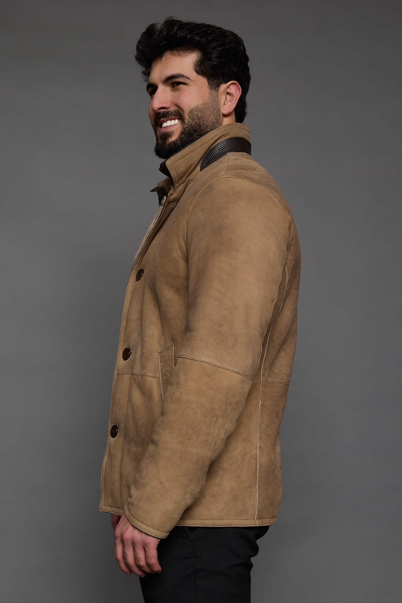 profile of a man in a tan coat against a grey background