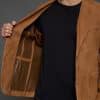 man holding open a tan jacket against a grey background