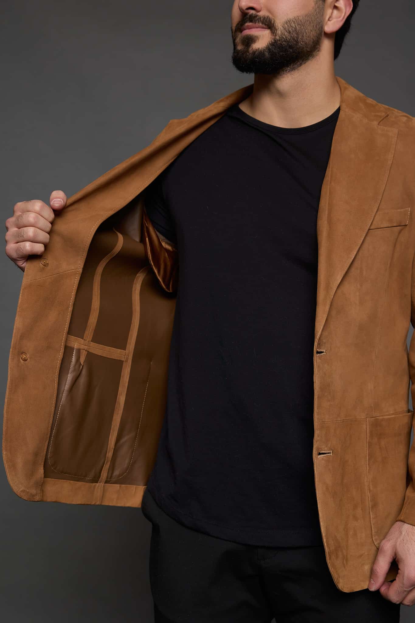 man holding open a tan jacket against a grey background