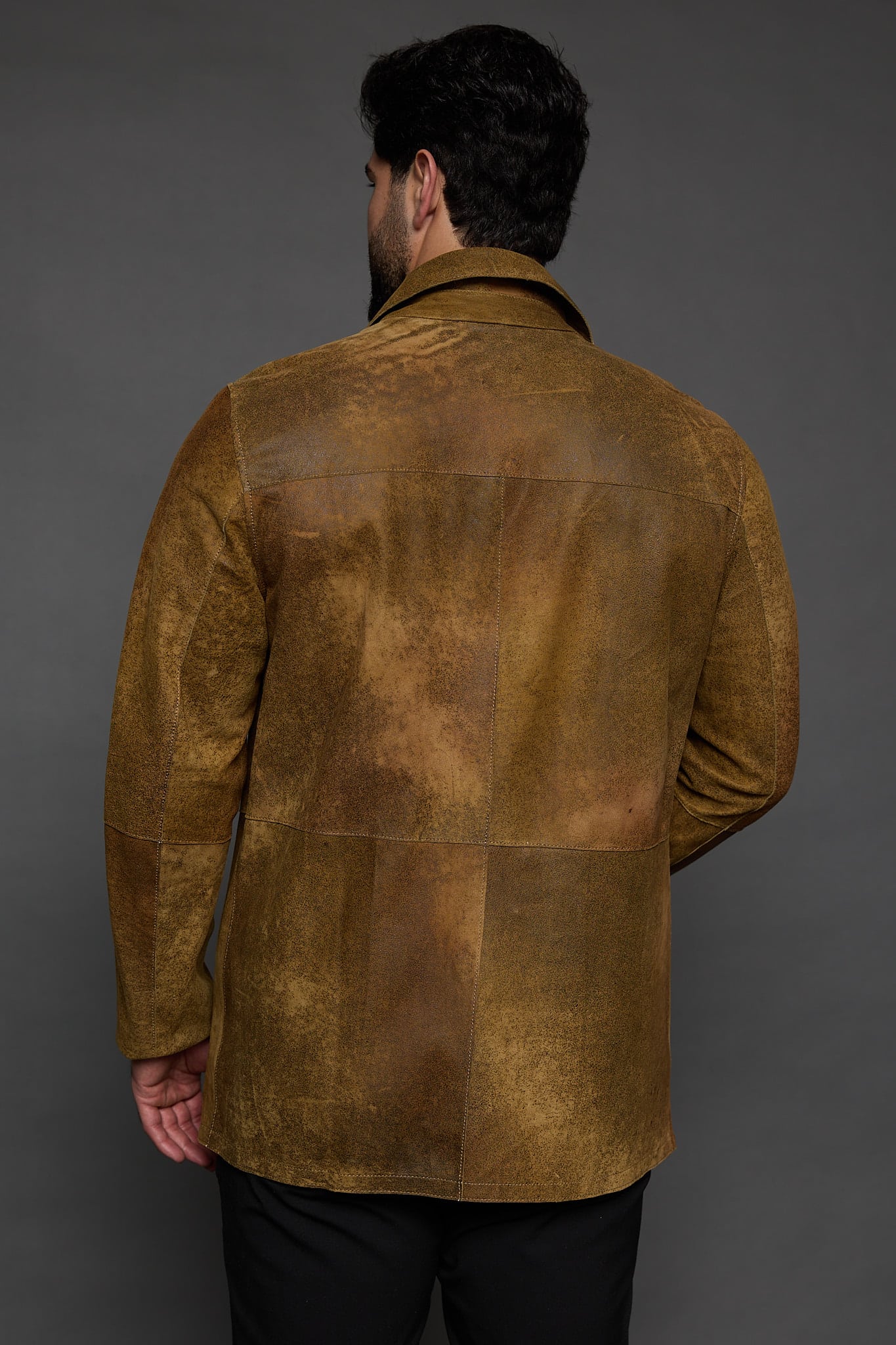 the back of a man in a brown jacket against a grey background