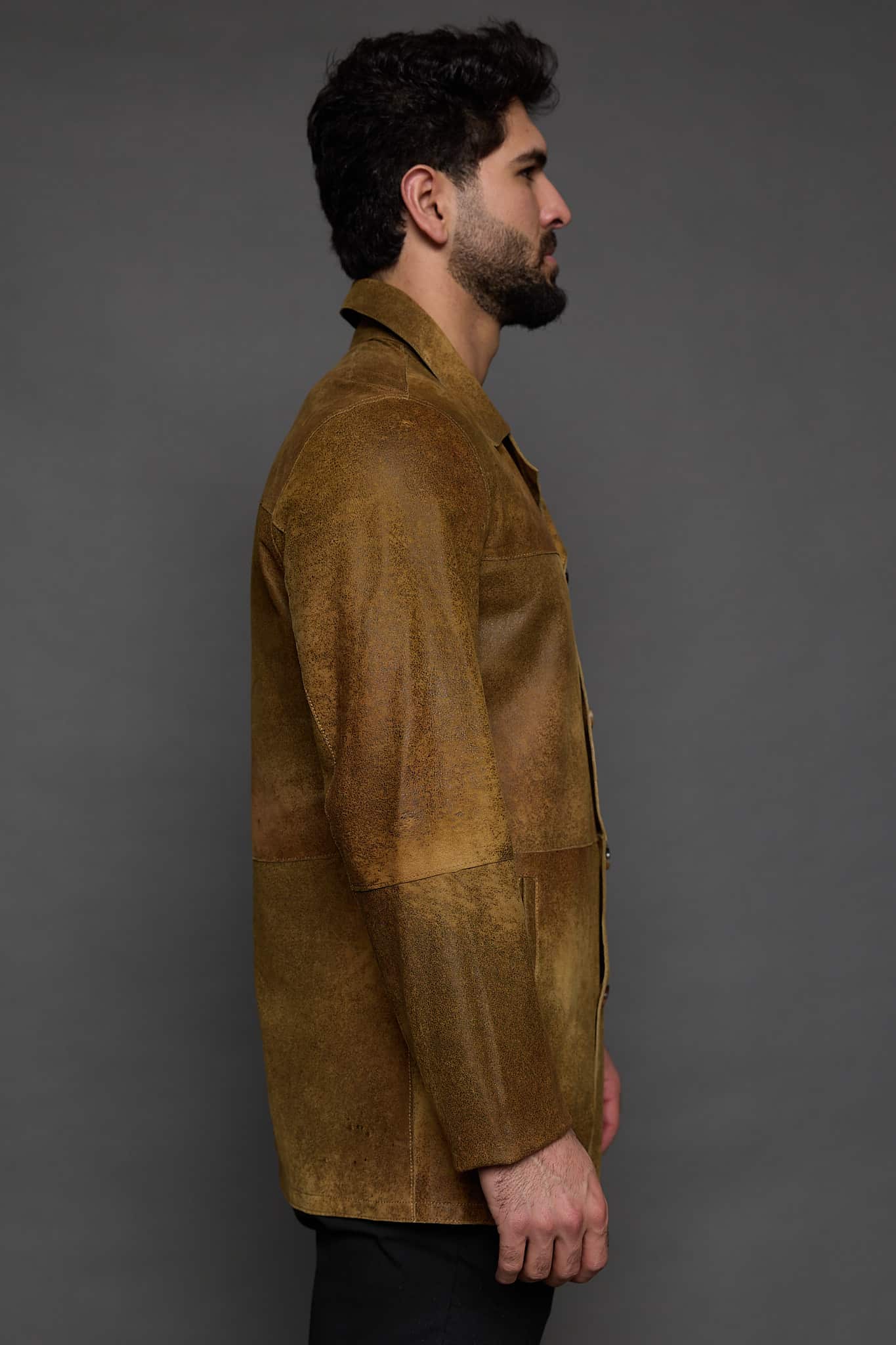 profile of a man in a brown jacket against a grey background
