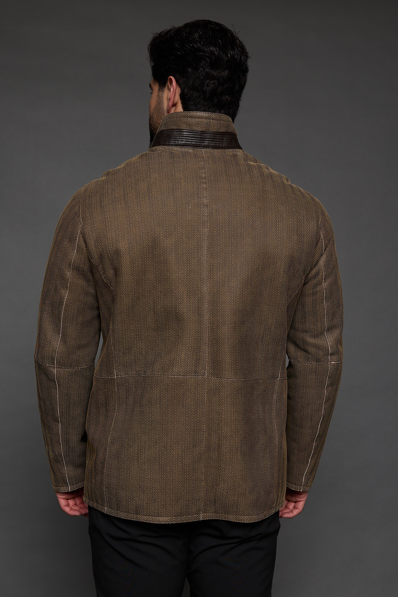 the back of a man in tan jacket against a grey background
