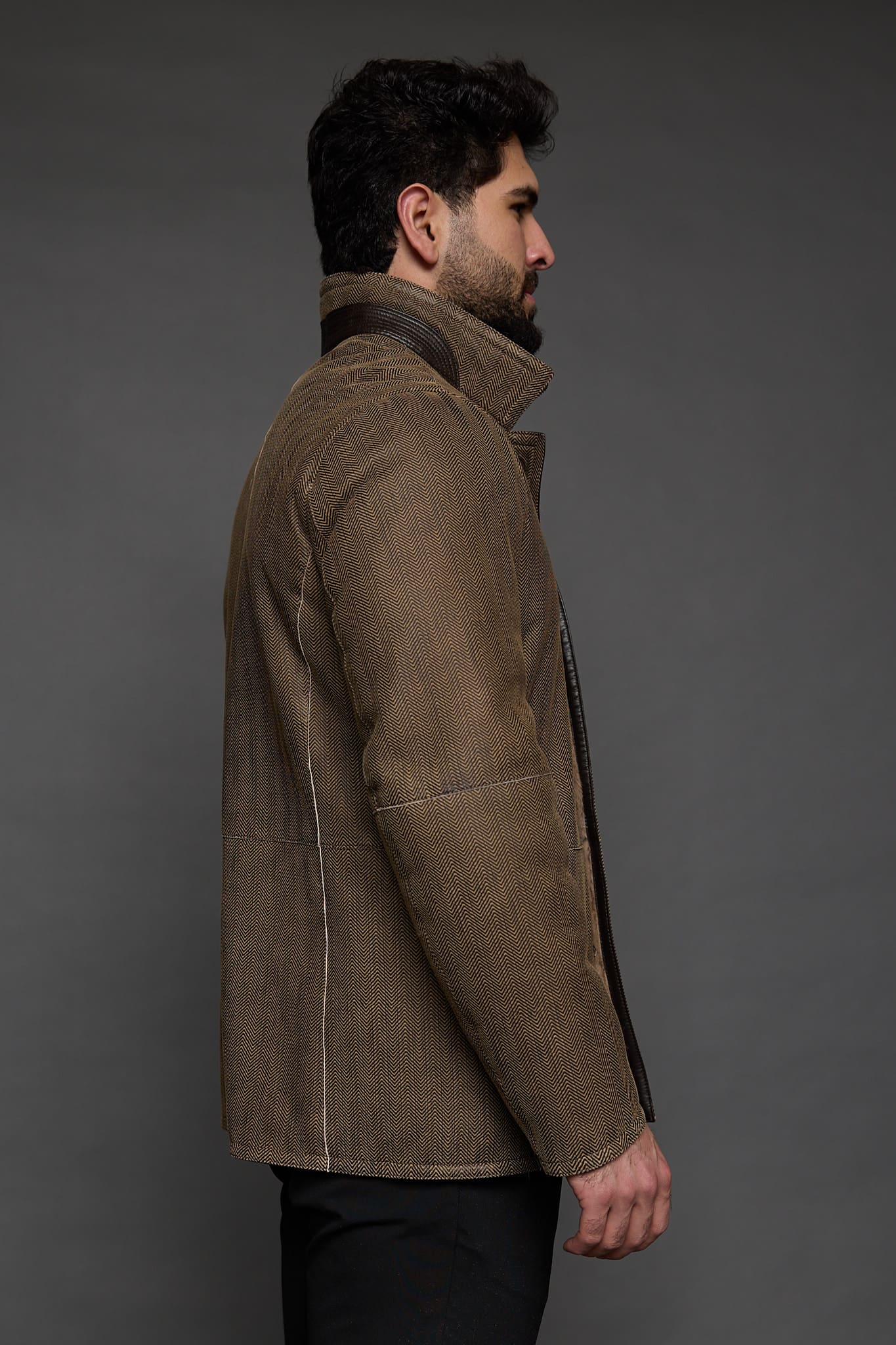 the profile of a man in tan jacket against a grey background