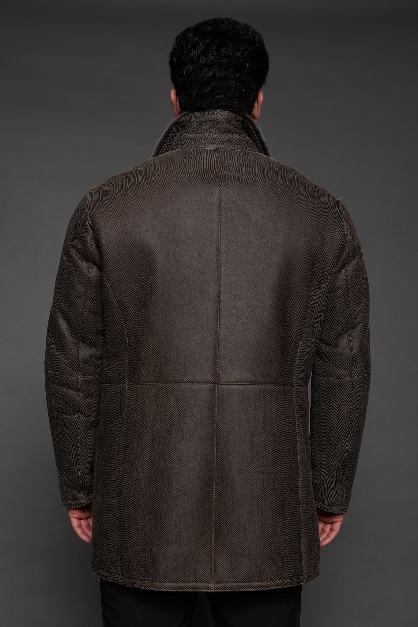 the back of a man in a brown coat against a grey background