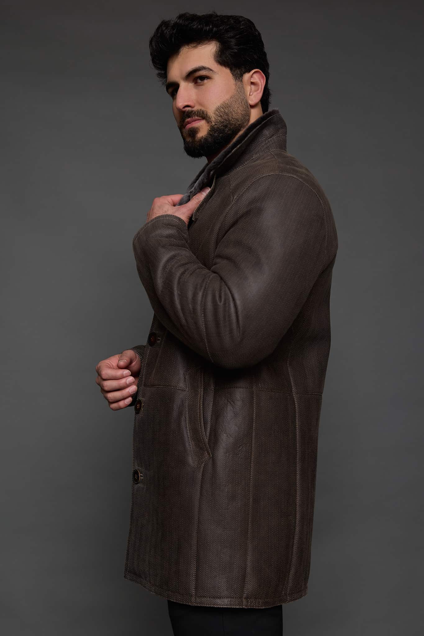 the profile of a man in a brown coat against a grey background