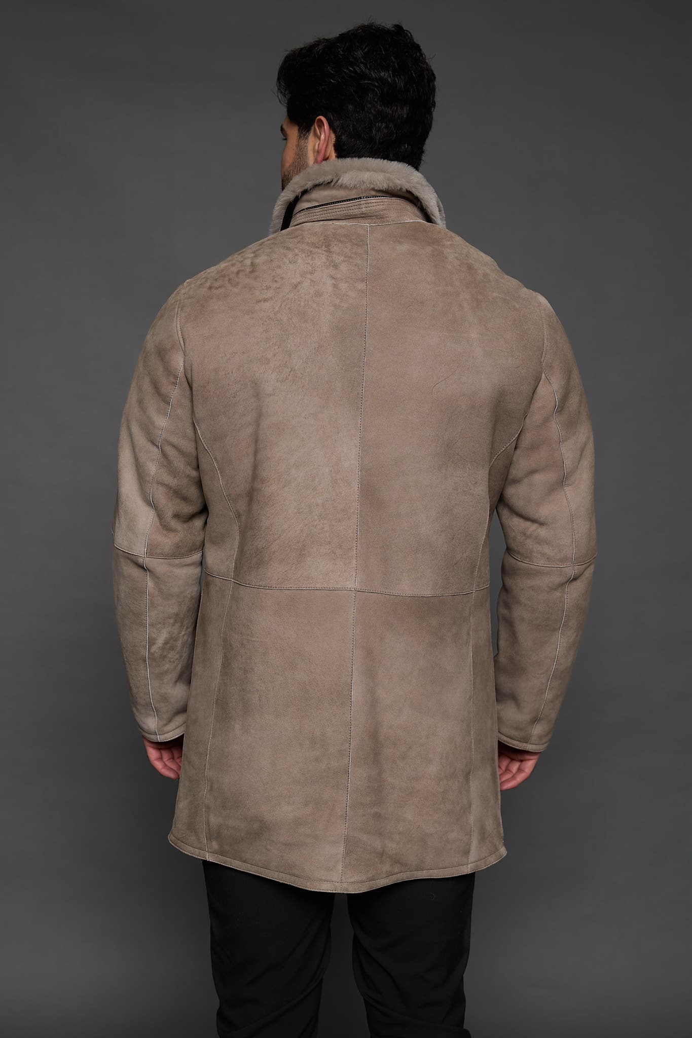 the back of a man in a tan coat against a grey background