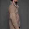 the side of a man in a tan coat against a grey background