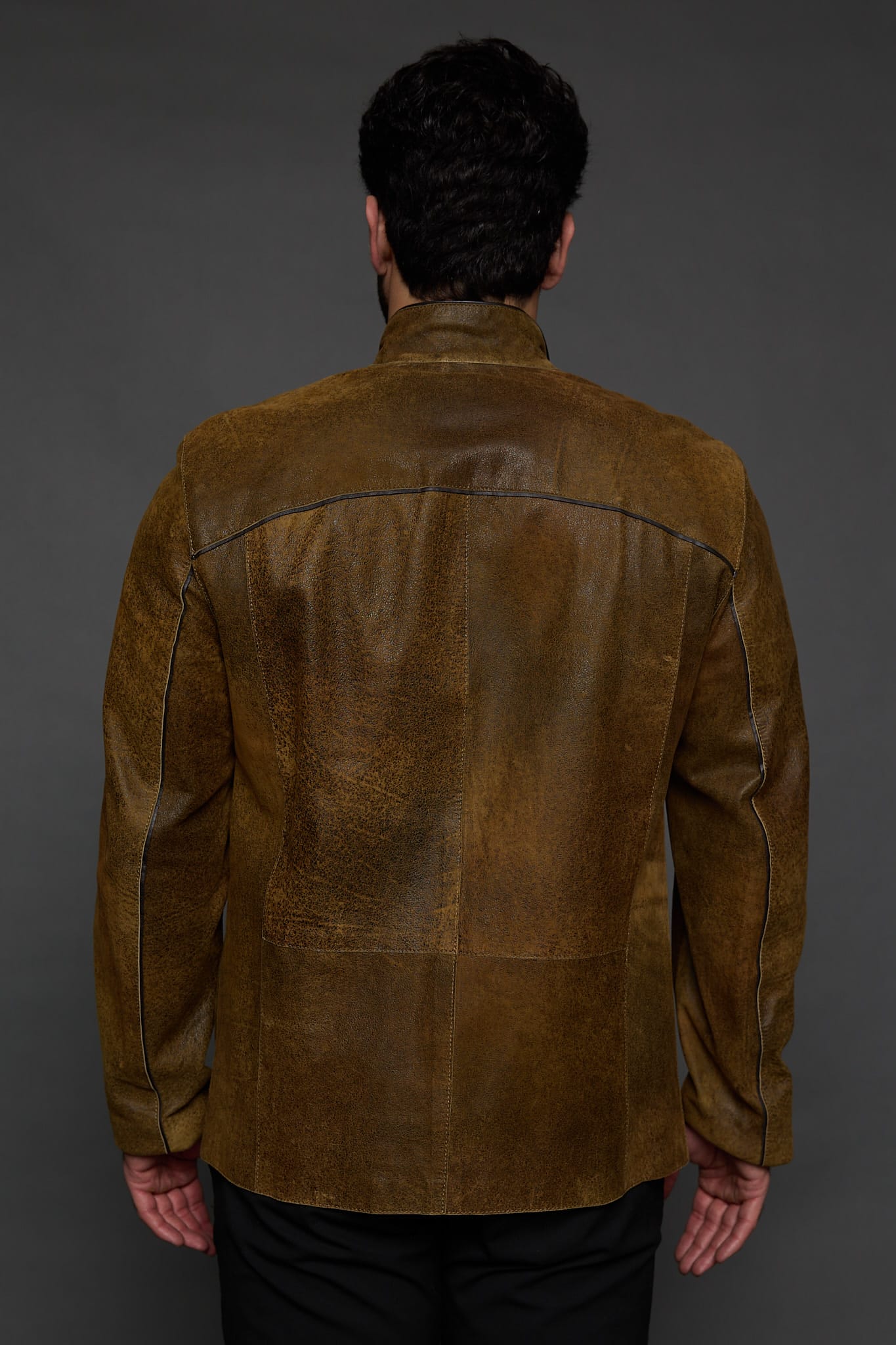 the back of a man in a brown jacket against a grey background