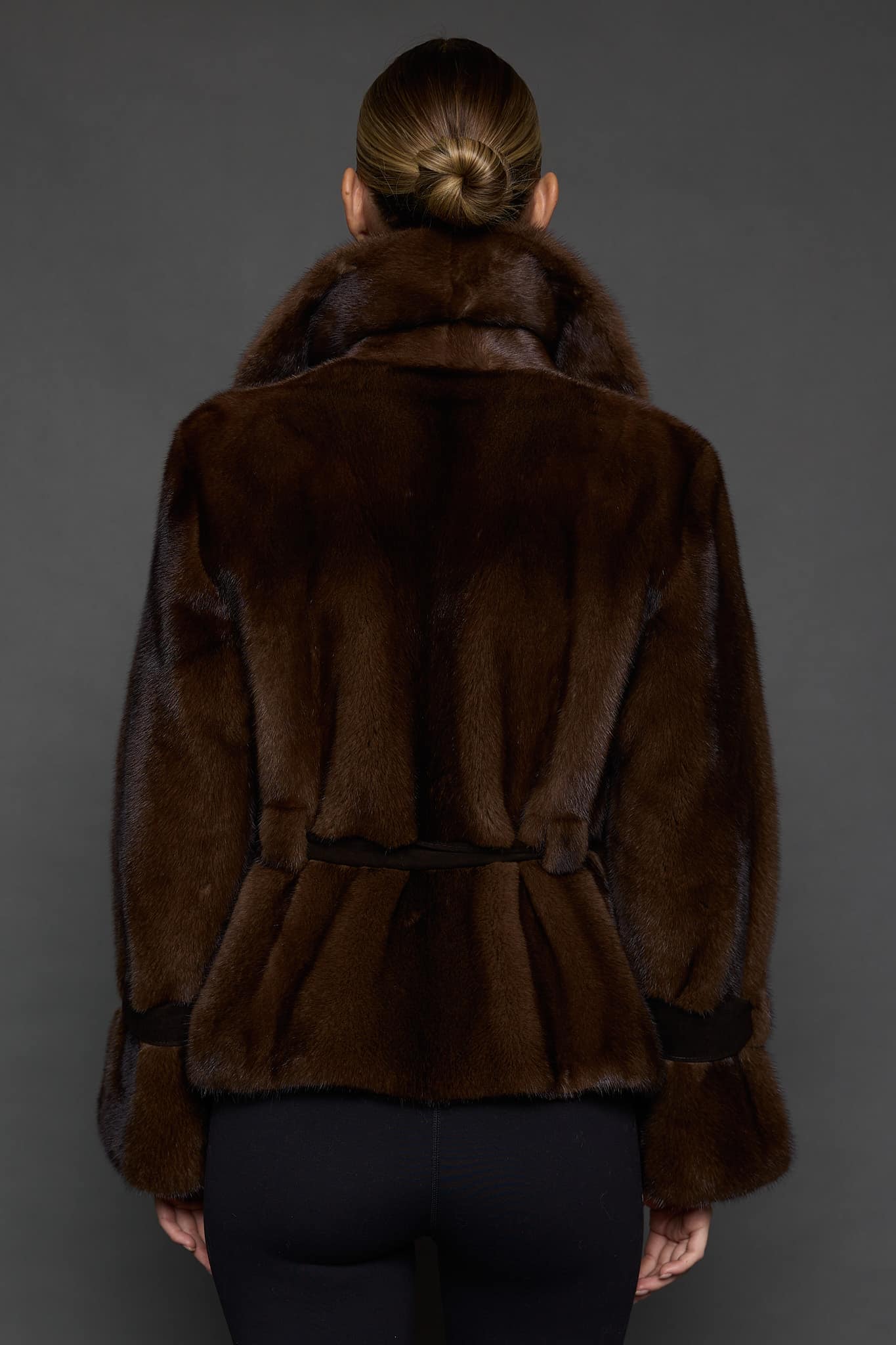 Reverse angle of a woman in a mahogany mink jacket facing a dark grey background