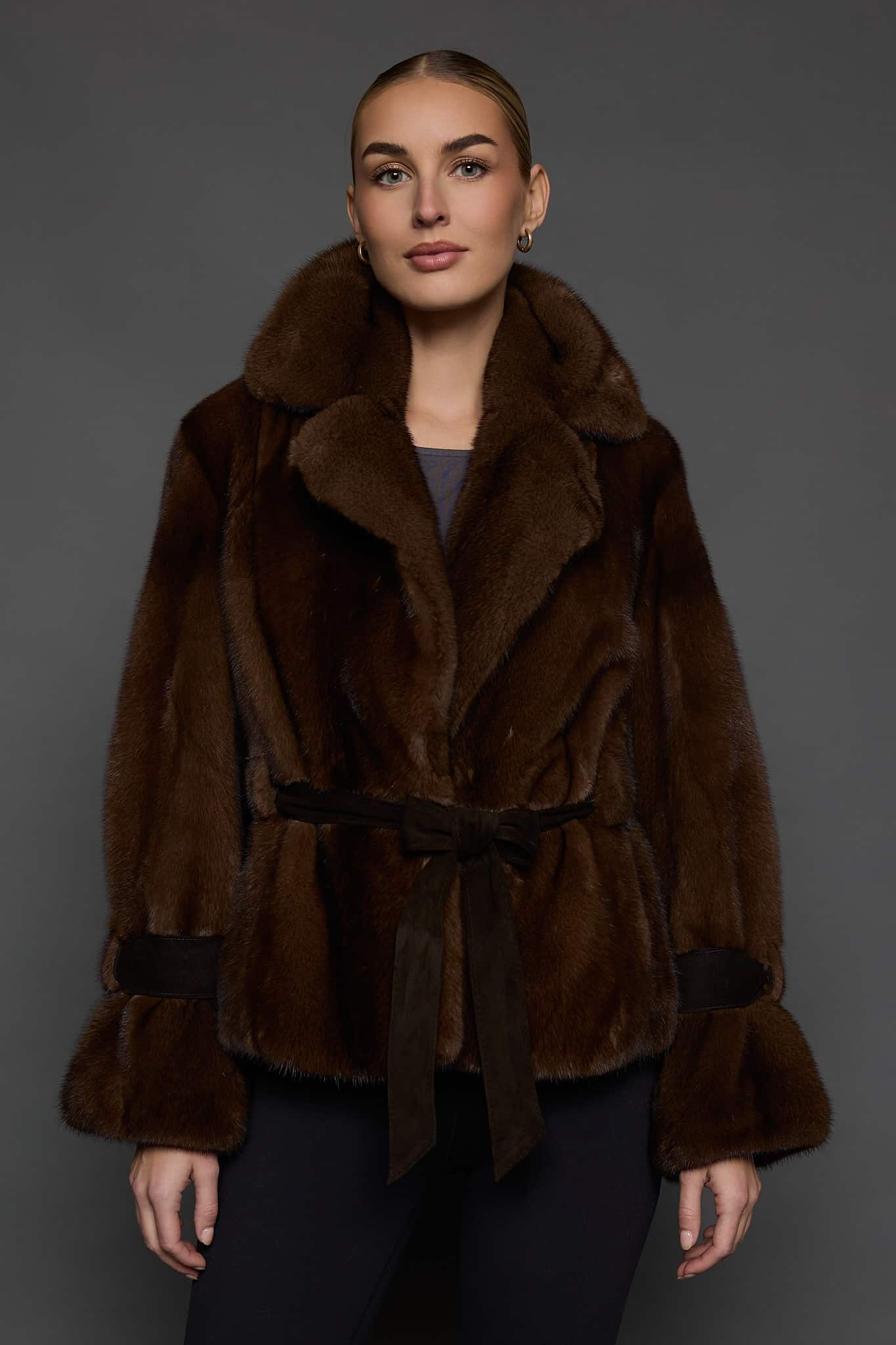 Frontal shot of a woman in a mahogany mink jacket standing against a dark grey background