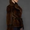 Profile shot of a woman in a mahogany mink jacket standing against a dark grey background
