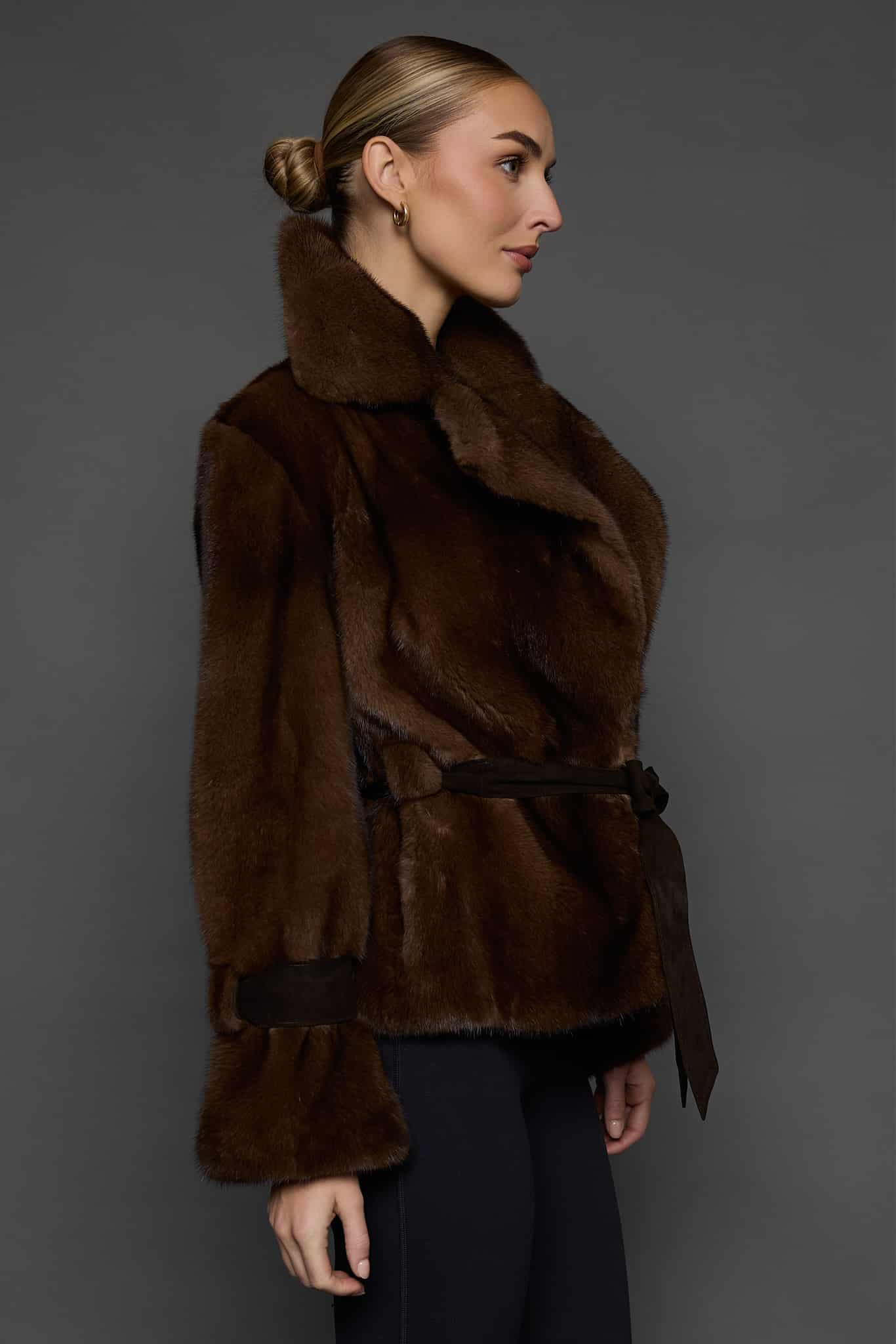 Profile shot of a woman in a mahogany mink jacket standing against a dark grey background