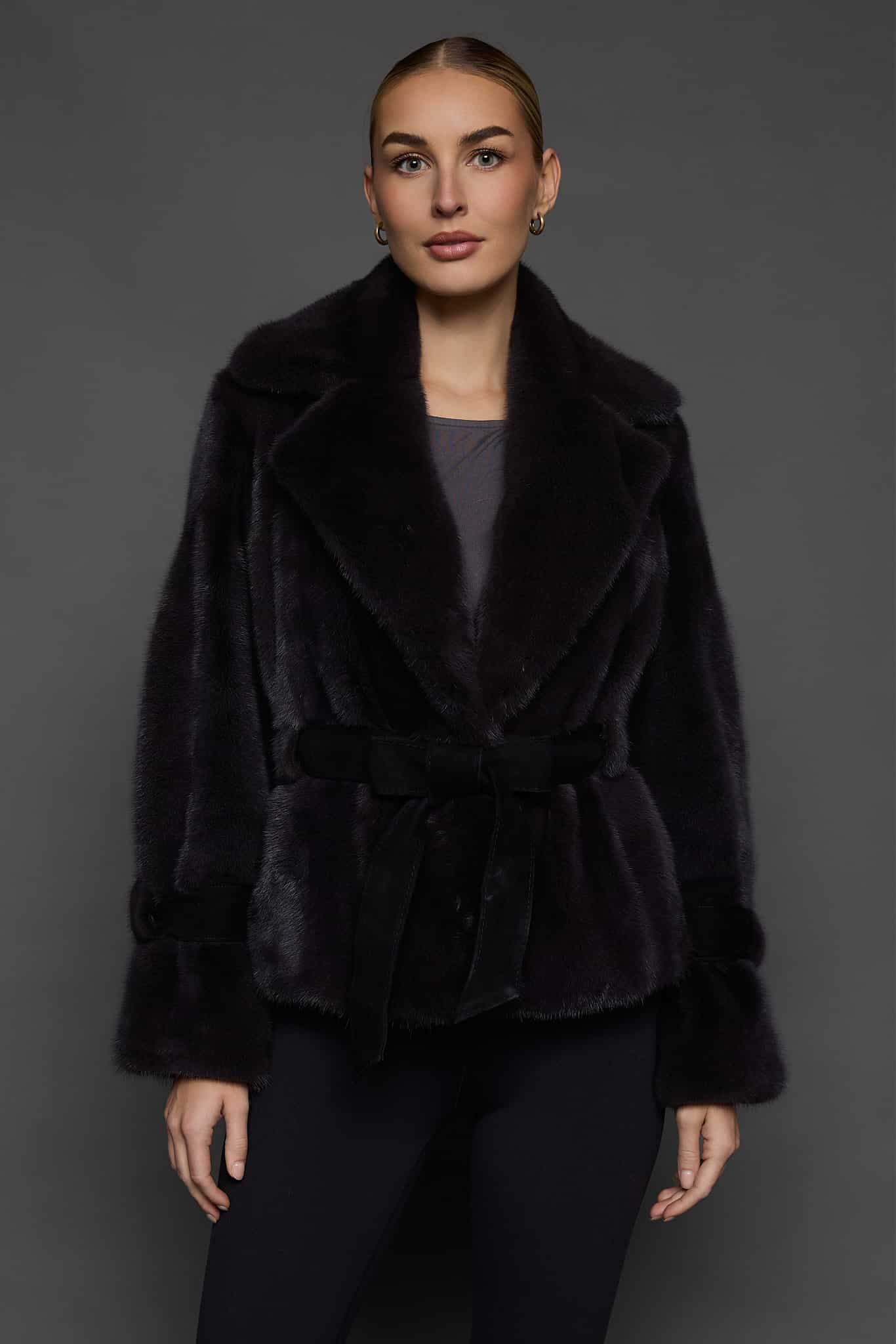 Frontal shot of a woman in a sapphire mink jacket standing against a dark grey background