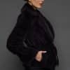 Profile shot of a woman in a sapphire mink jacket with her right hand in the pocket standing against a dark grey background