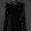 Rear view of a woman in a black mink jacket with the hood down standing in front of a dark grey background