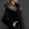 Profile view of a woman in a black mink jacket with the hood down standing in front of a dark grey background