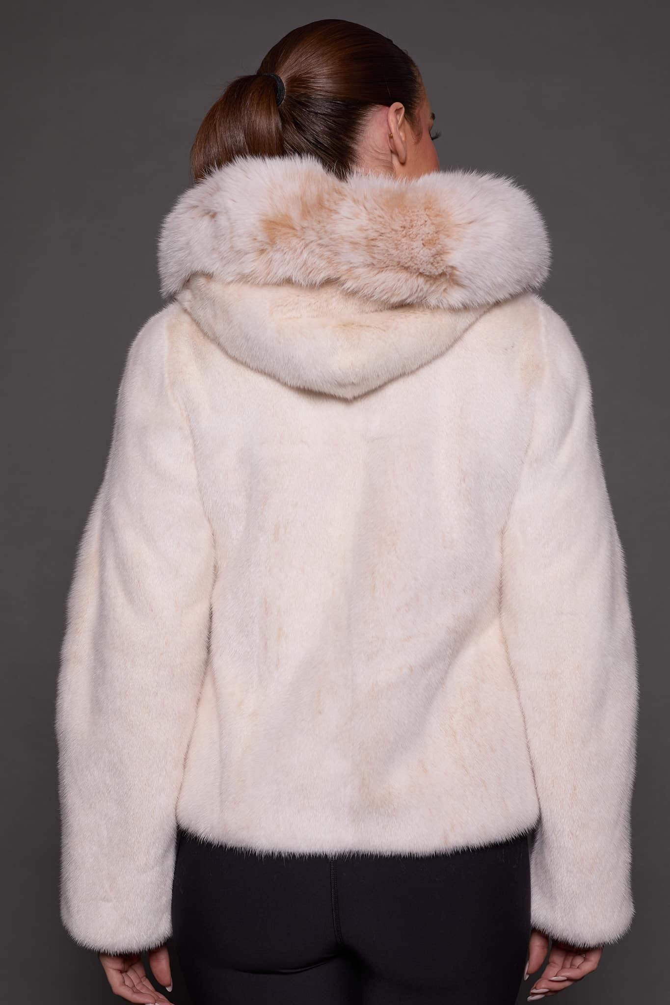 the back of a woman in a white fur jacket against a grey background
