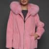 Frontal view of a woman in a blush mink jacket with the hood down standing in front of a dark grey background