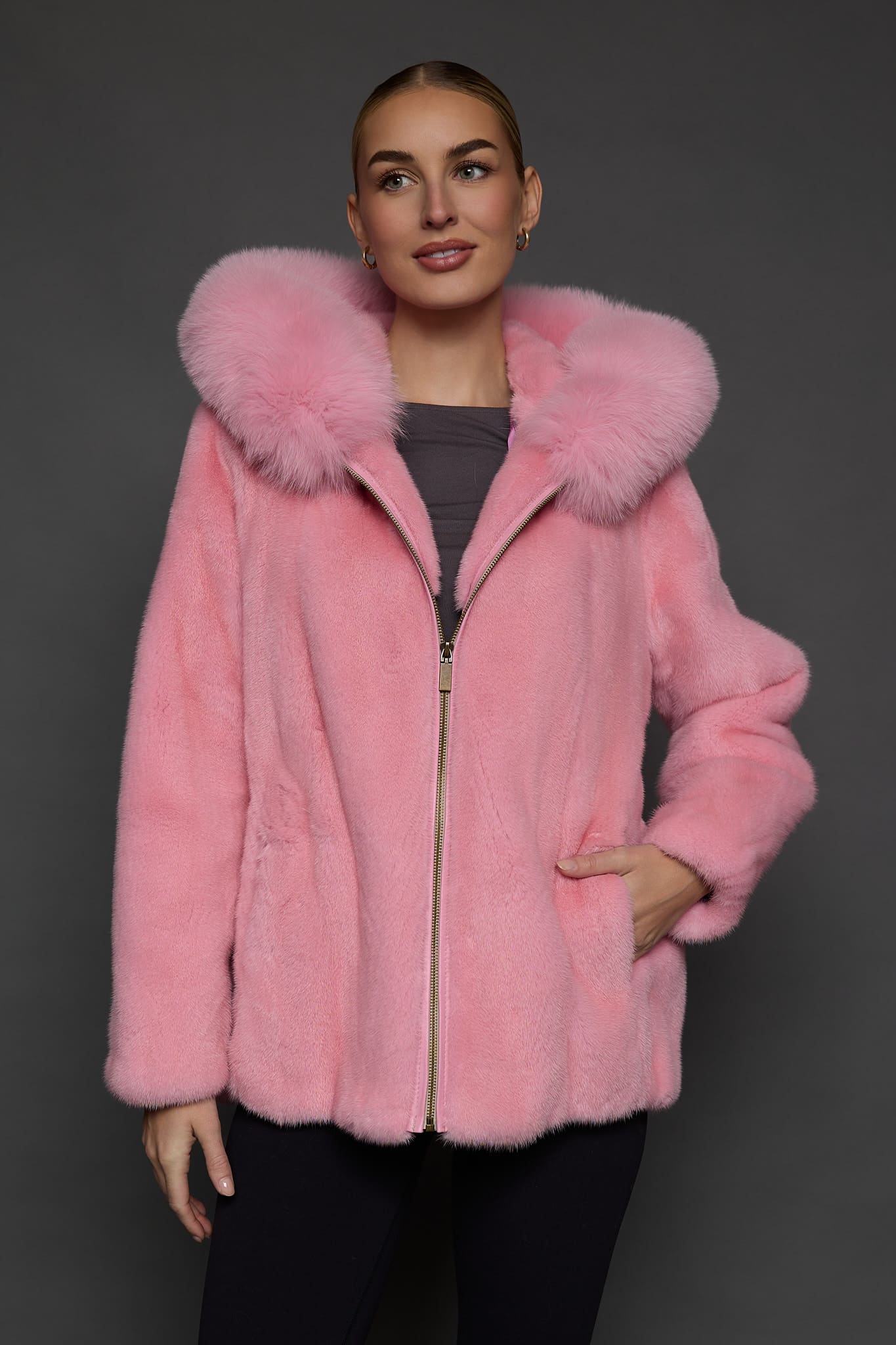 Frontal view of a woman in a blush mink jacket with the hood down standing in front of a dark grey background
