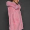 Profile view of a woman in a blush mink jacket with the hood down standing in front of a dark grey background