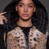 ANDI LYNX PUFFER VEST BLACK HOOD Up close image of a woman in a black and brown fur vest against a grey background with a black hood over her head