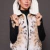 Andi Lynx Puffer Vest White Hood the front of a woman wearing a white puffer vest with lynx fur holding up the hood against a solid grey background