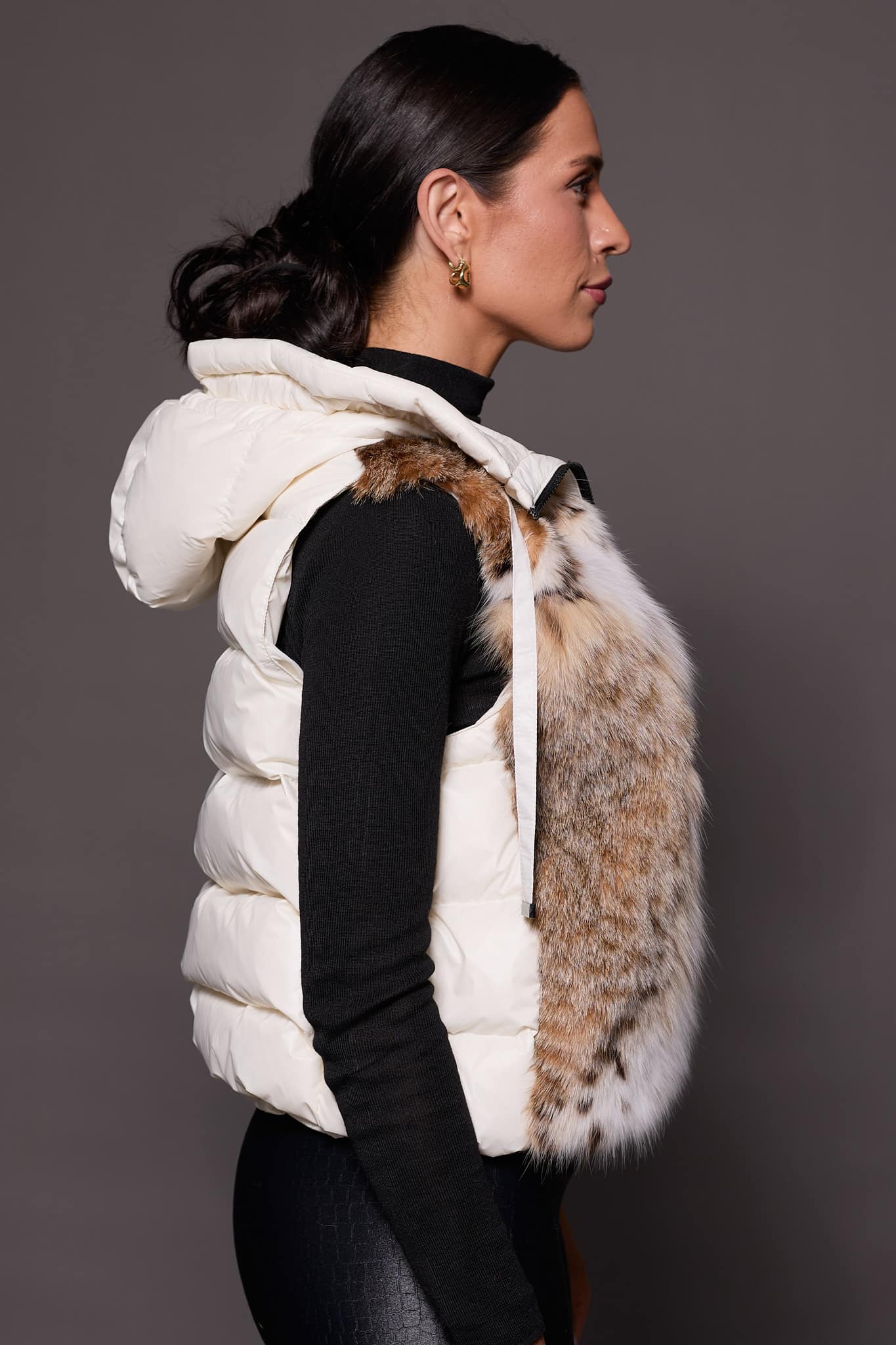 Andi Lynx Puffer Vest White Side the side profile of a woman wearing a white puffer vest with lynx fur against a solid grey background
