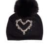 A black beanie with a heart graphic on it and a fox pom pom on top laying on a white background.