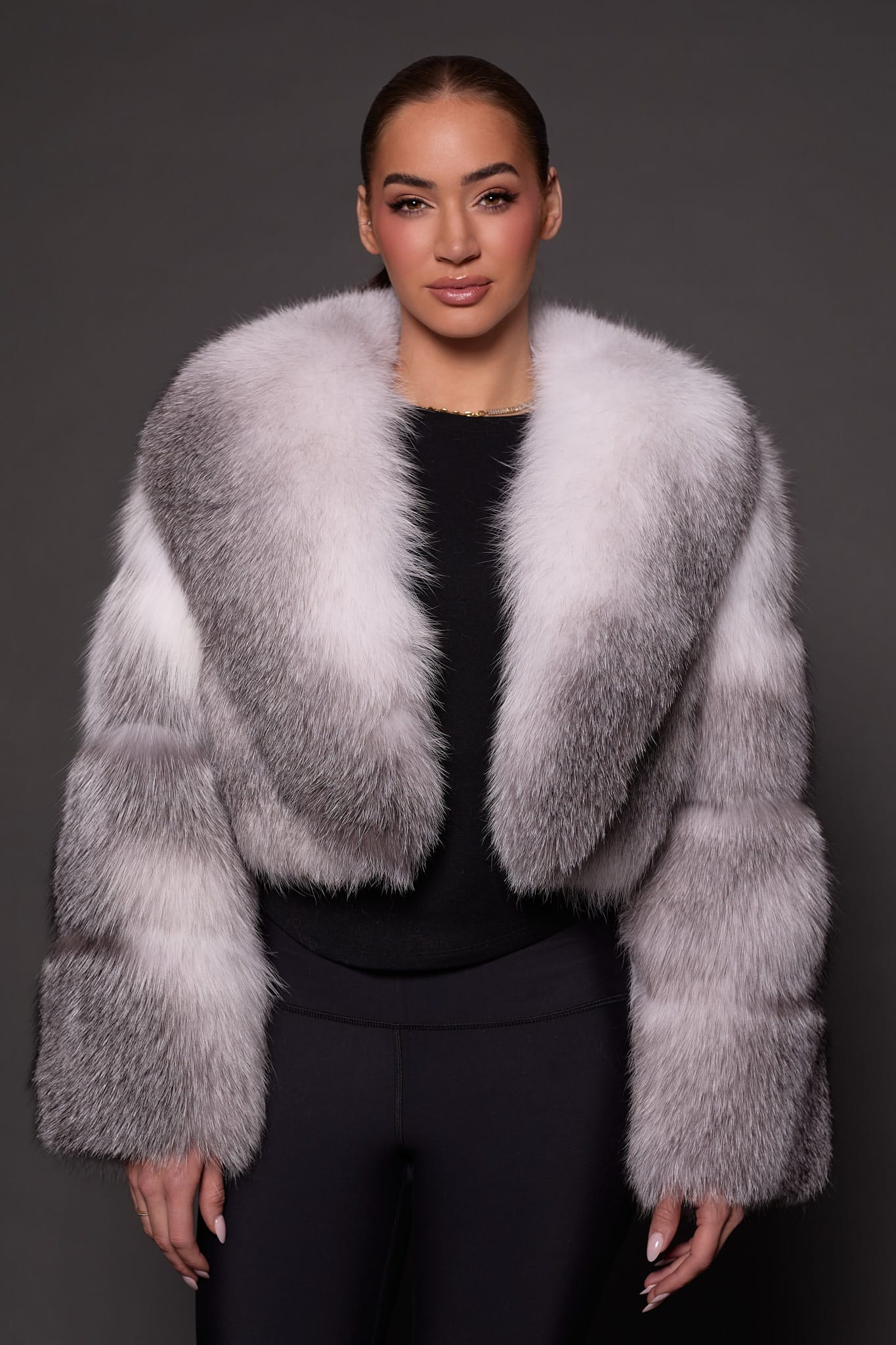 The front of woman in a white and grey fur jacket against a grey background