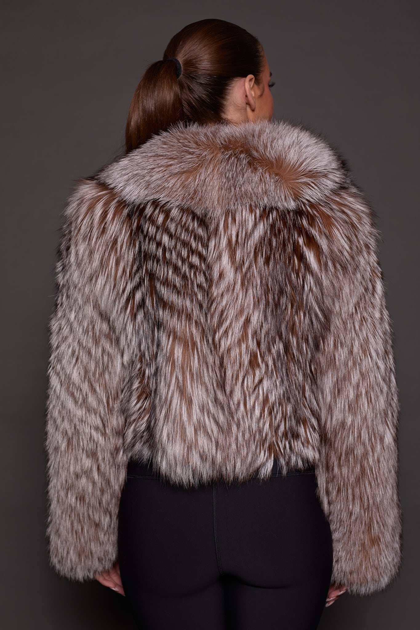 the back of a woman in a brown fur jacket against a grey background
