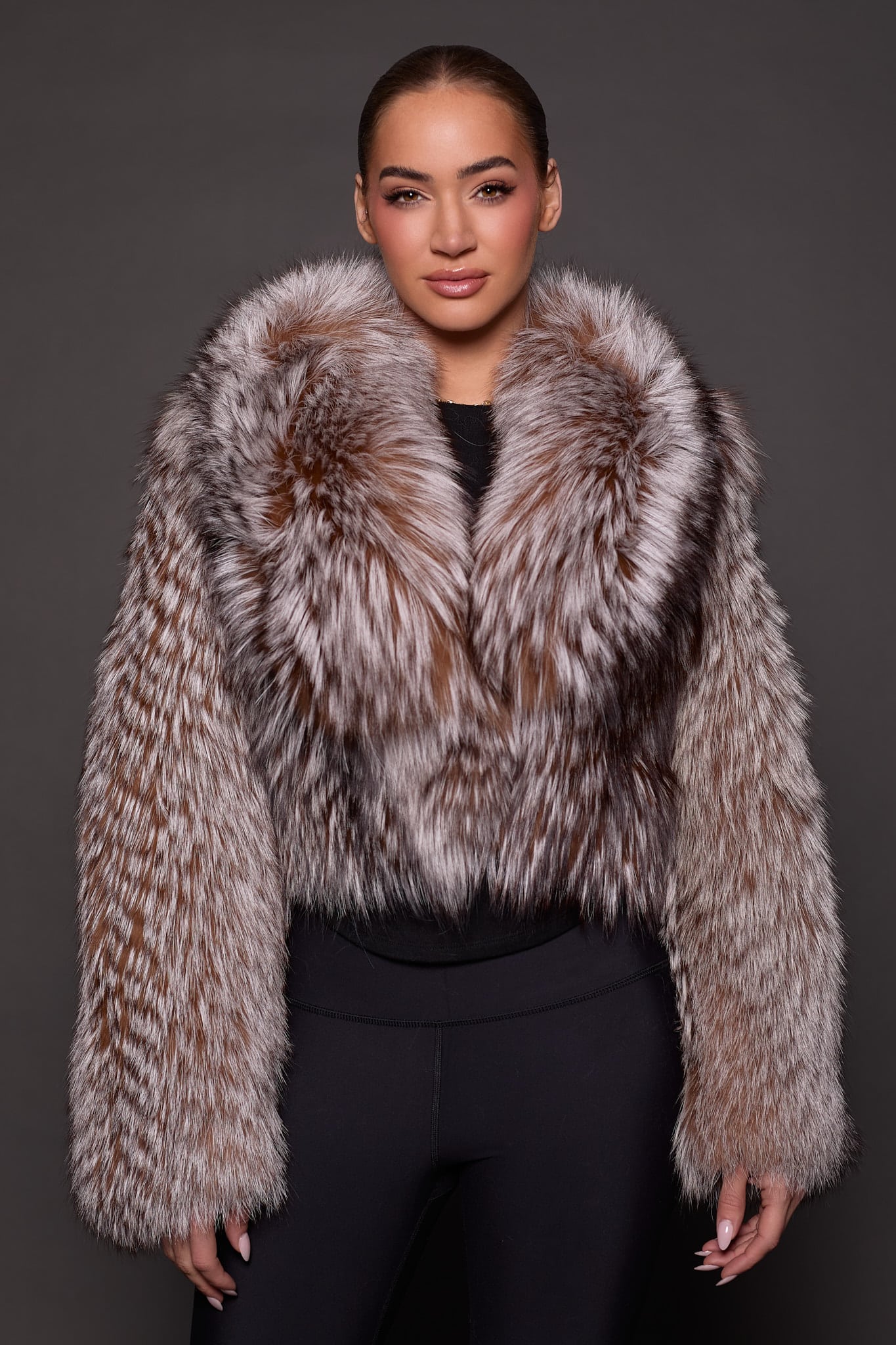 the front of a woman in a brown and white fur jacket against a grey background