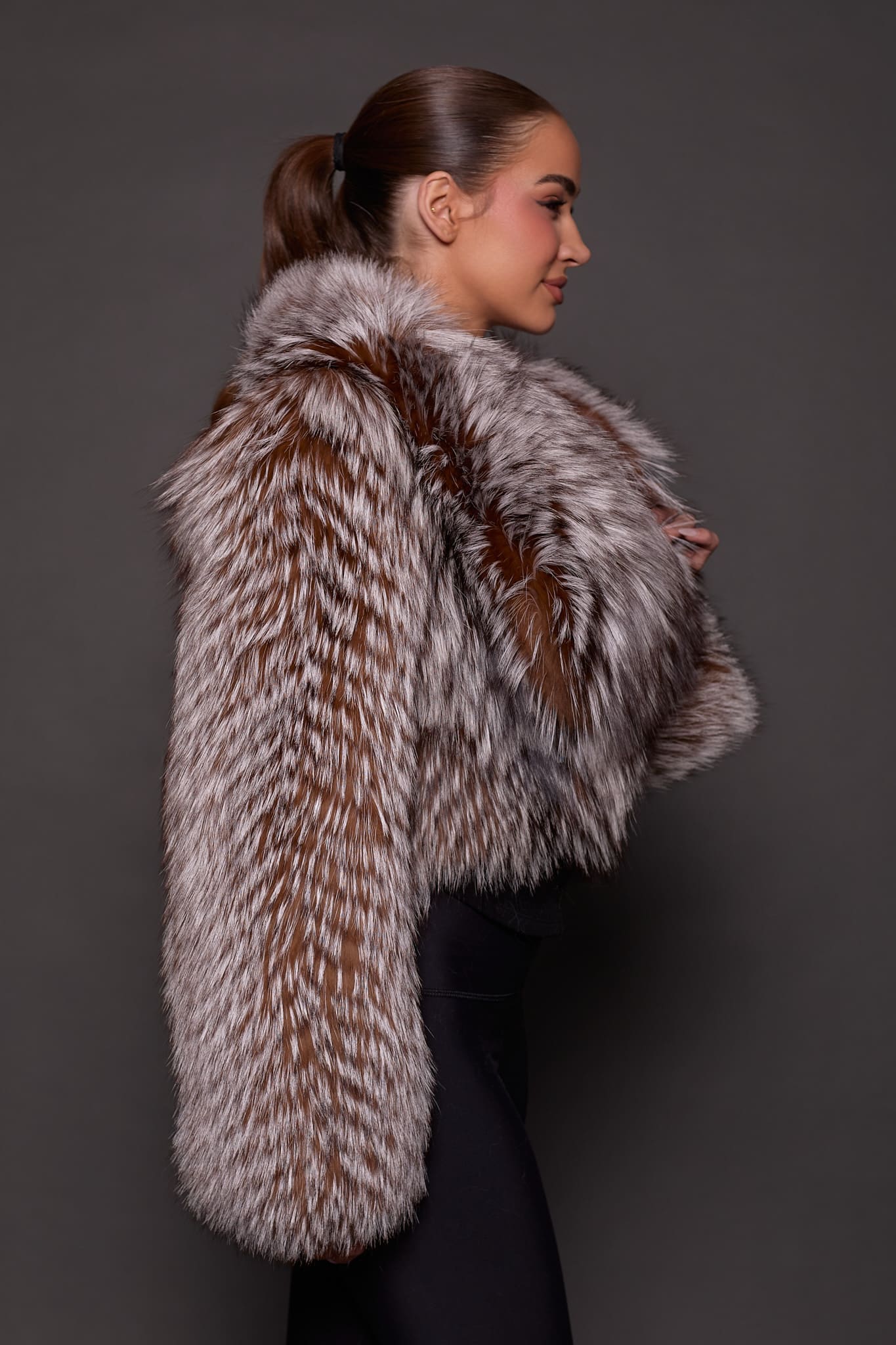 the side profile of a woman in a brown fur jacket against a grey background