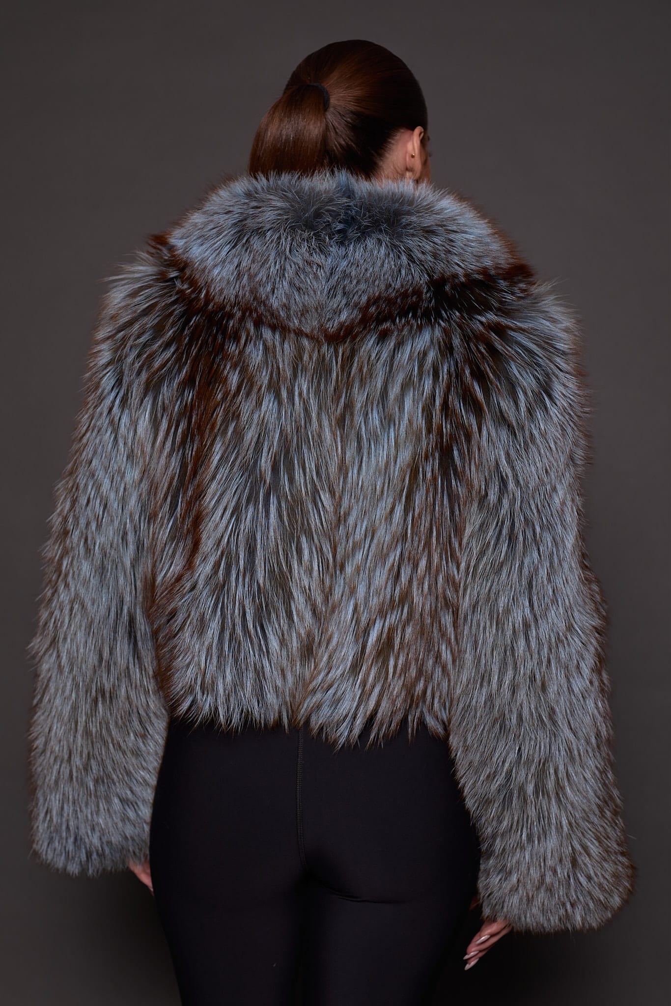 the back of a woman in a blue and grey fur jacket against a grey background
