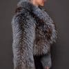 the side profile of a woman in a blue and grey fur jacket against a grey background