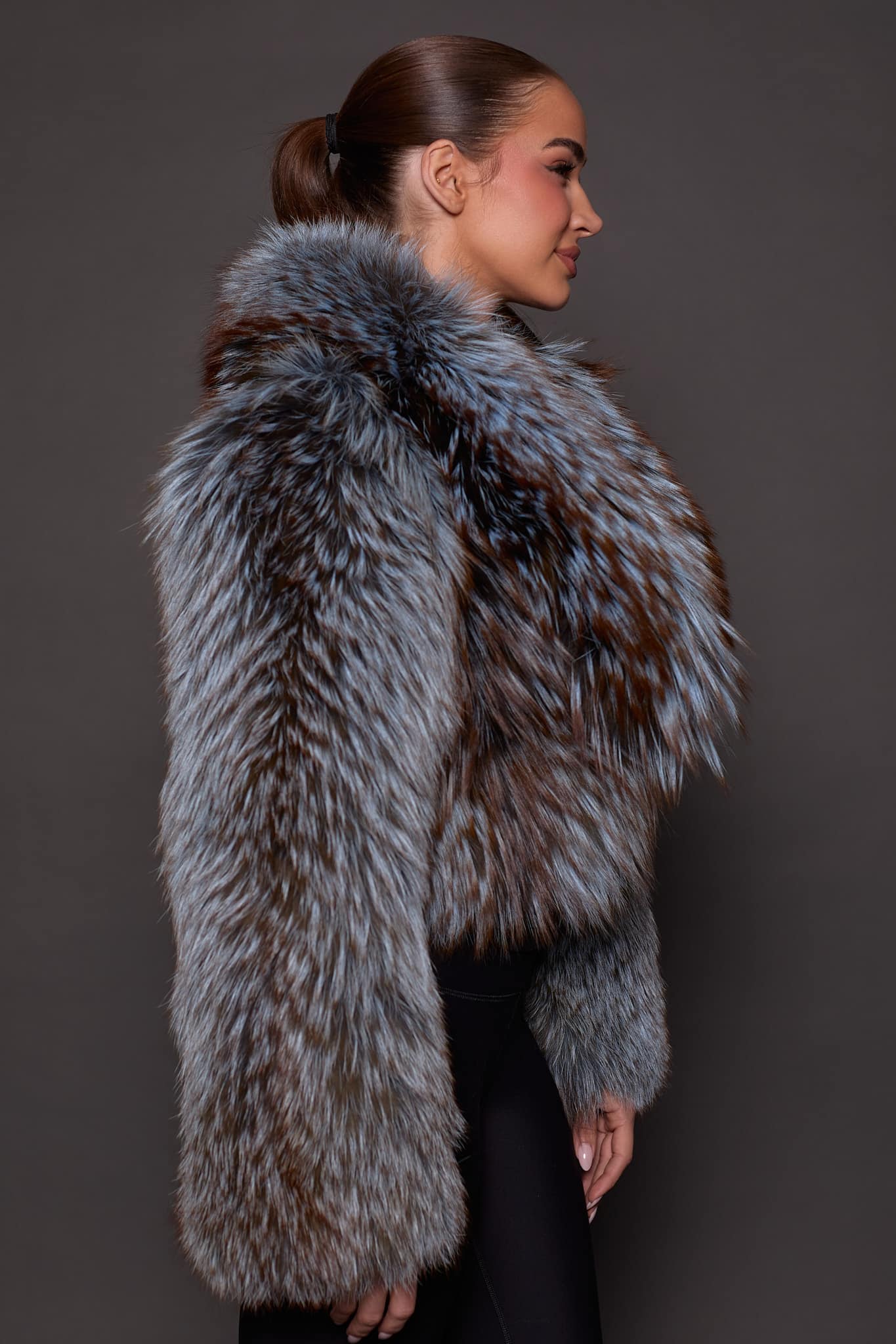 the side profile of a woman in a blue and grey fur jacket against a grey background