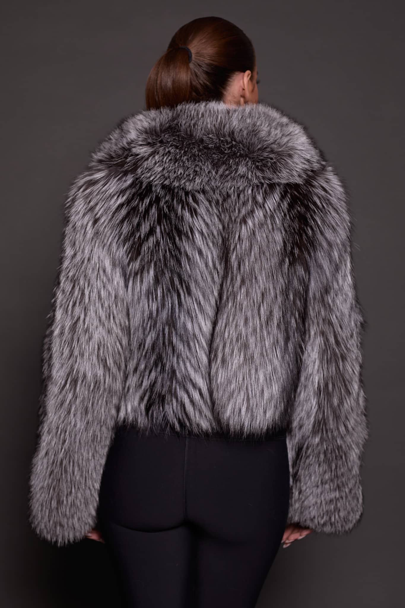 the back of a woman in a silver fur jacket against a grey background