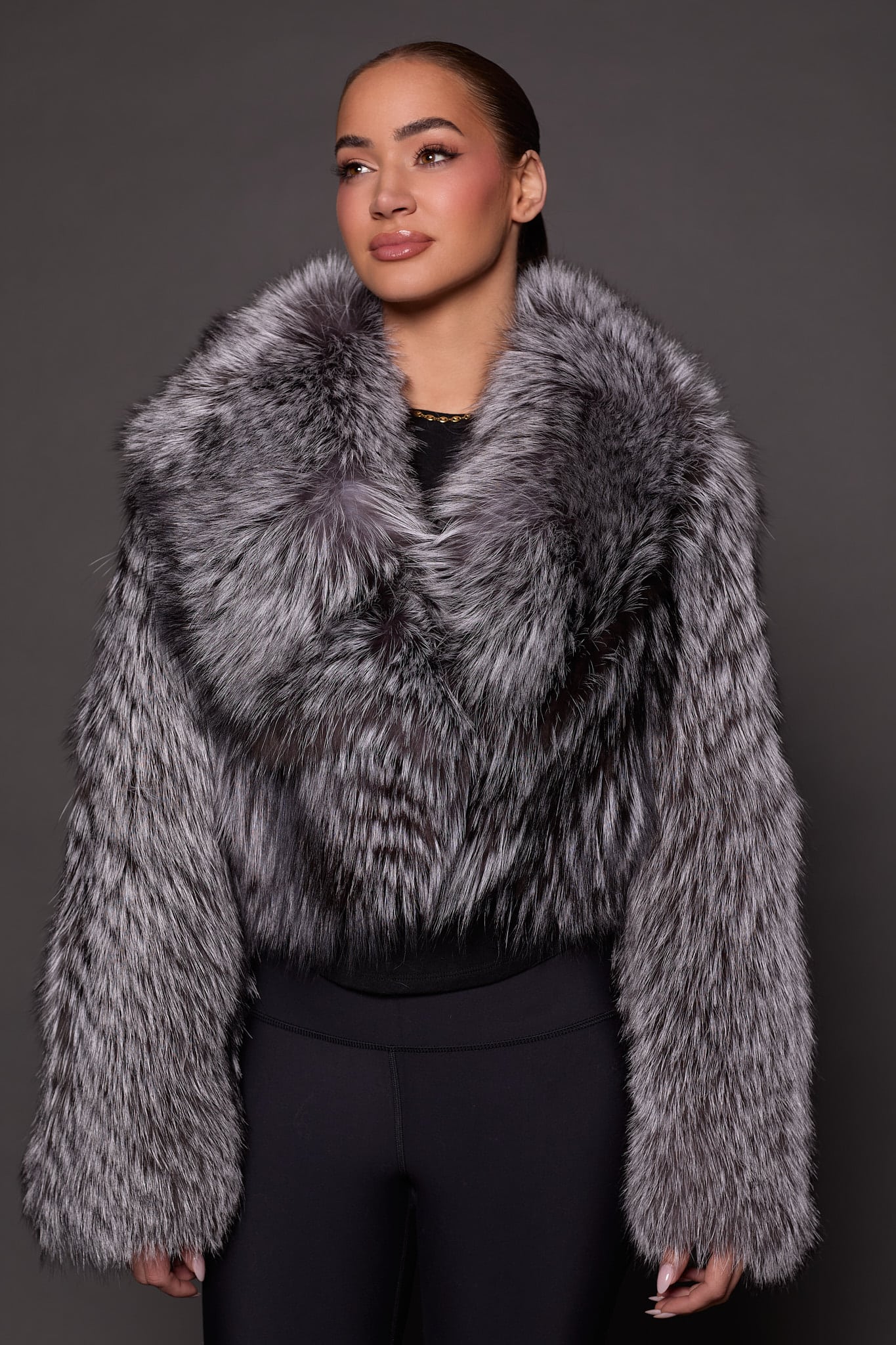 the front of a a woman in a silver fur jacket against a grey background