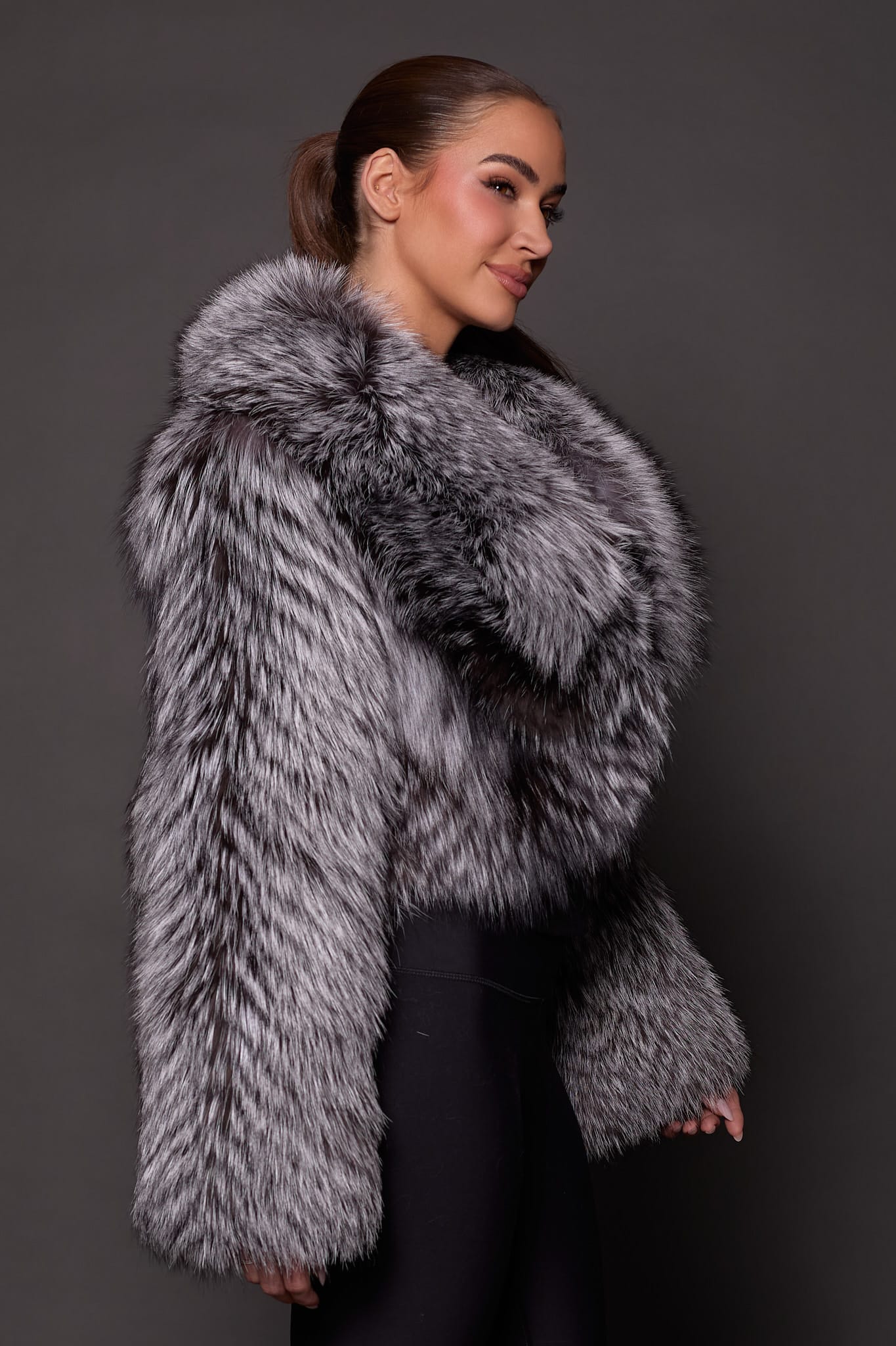 the side profile of a a woman in a silver fur jacket against a grey background