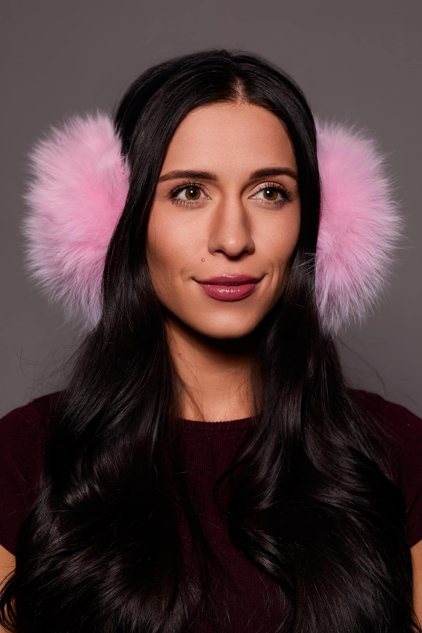 woman wearing pink earmuffs against a grey background