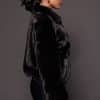 the side profile of a woman in a black mink jacket against a grey background