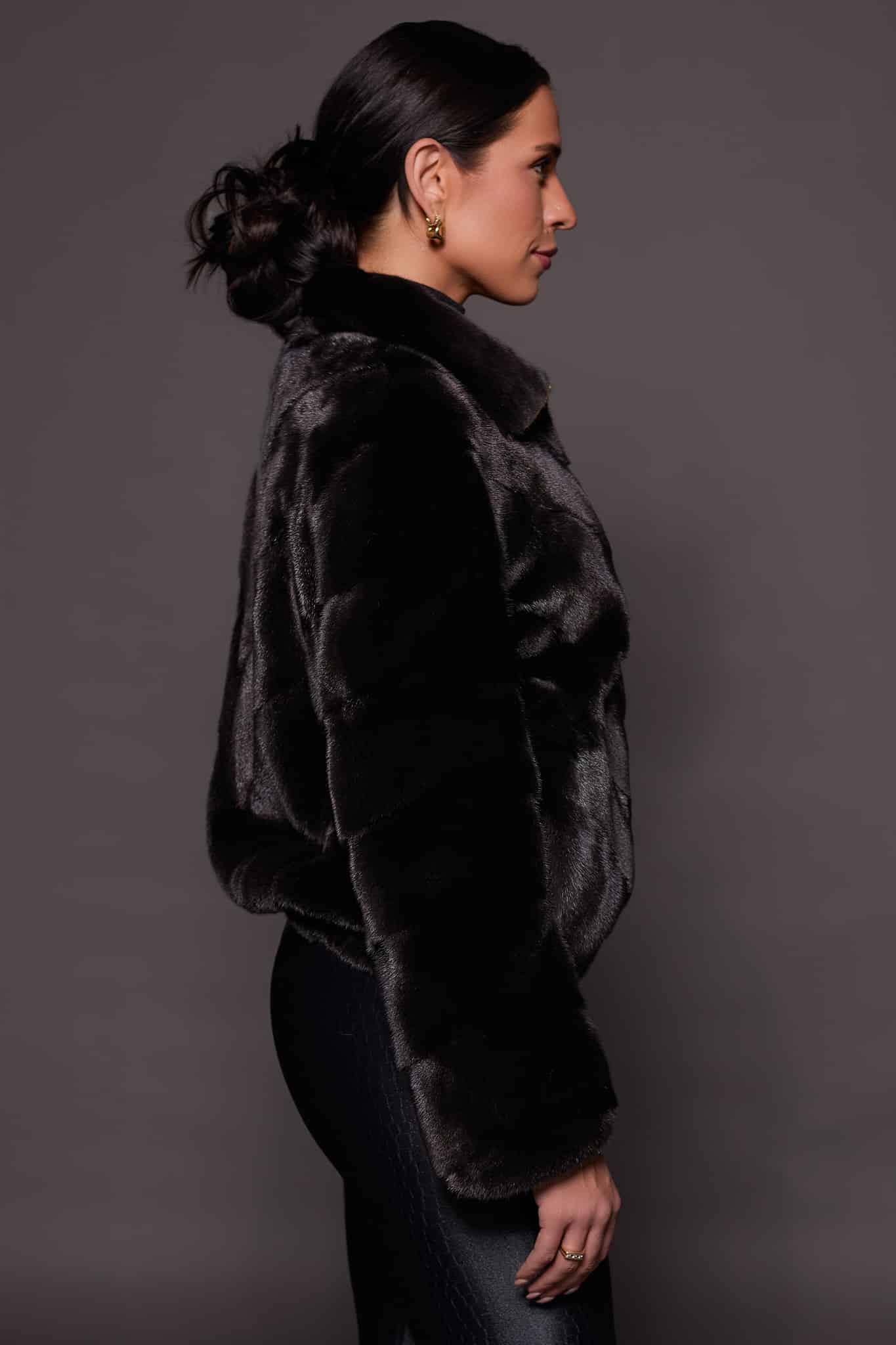 the side profile of a woman in a black mink jacket against a grey background