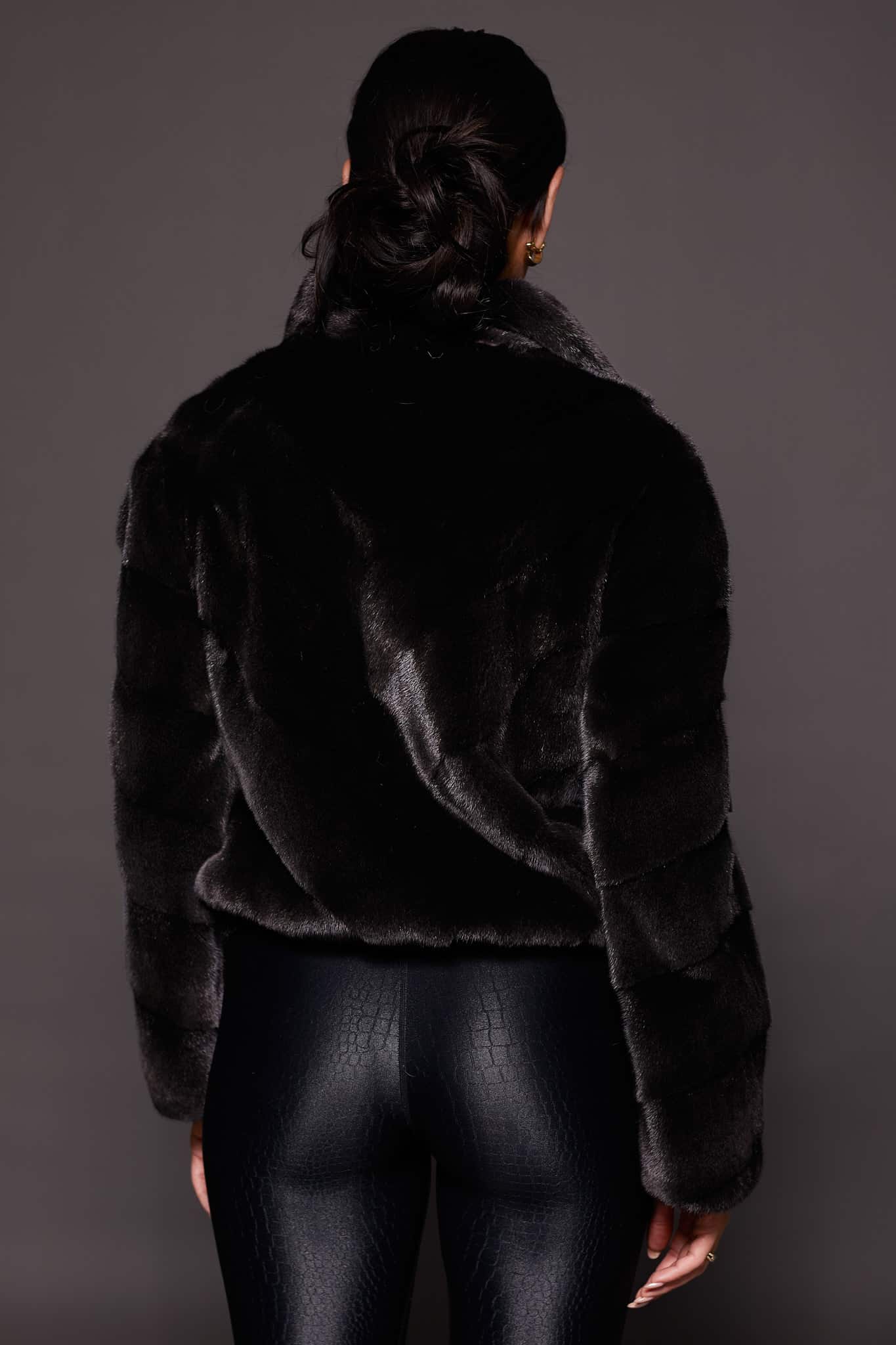 the back of a woman in a black mink jacket against a grey background