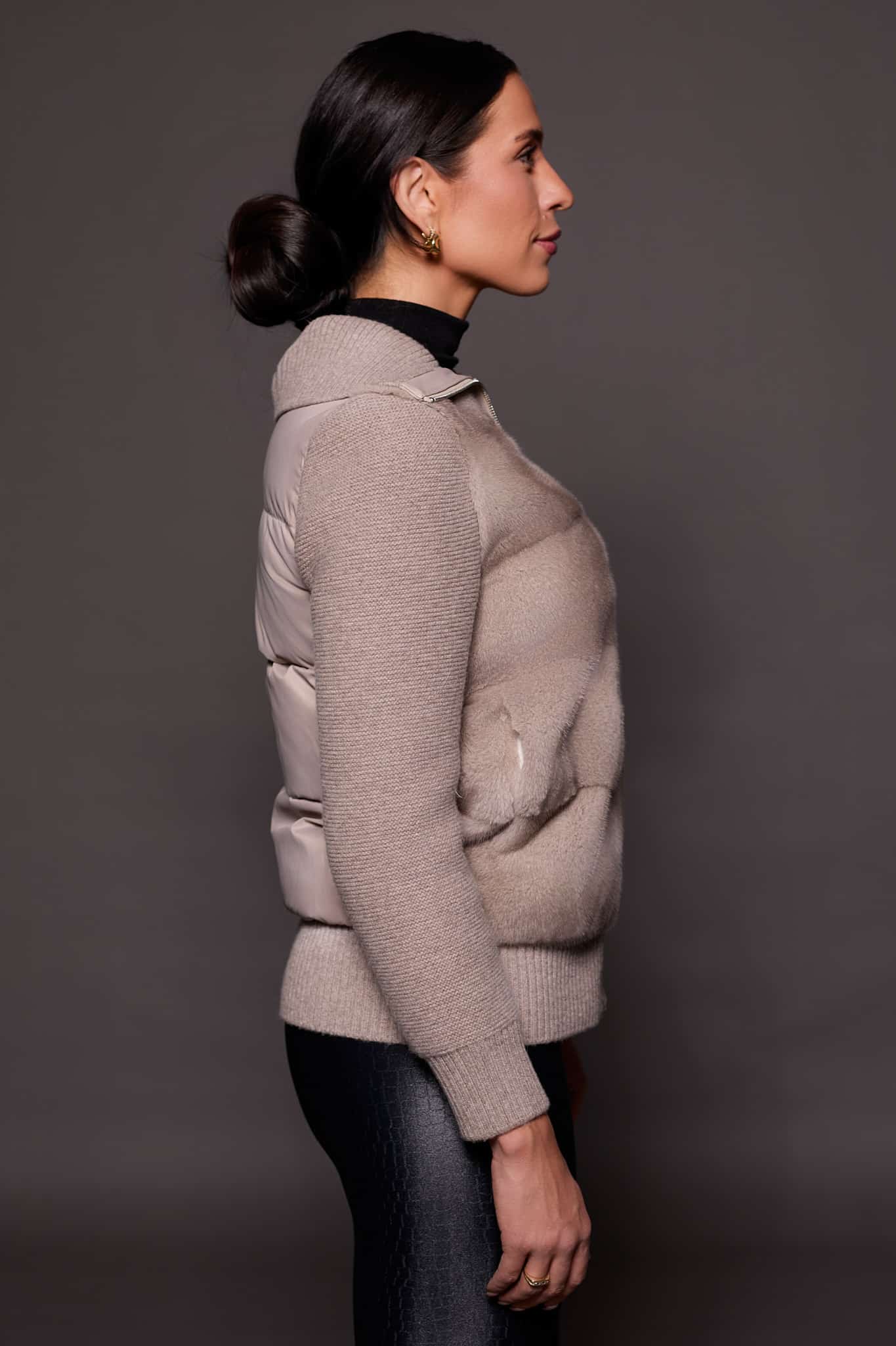 the side of a woman in a grey jacket against a grey background