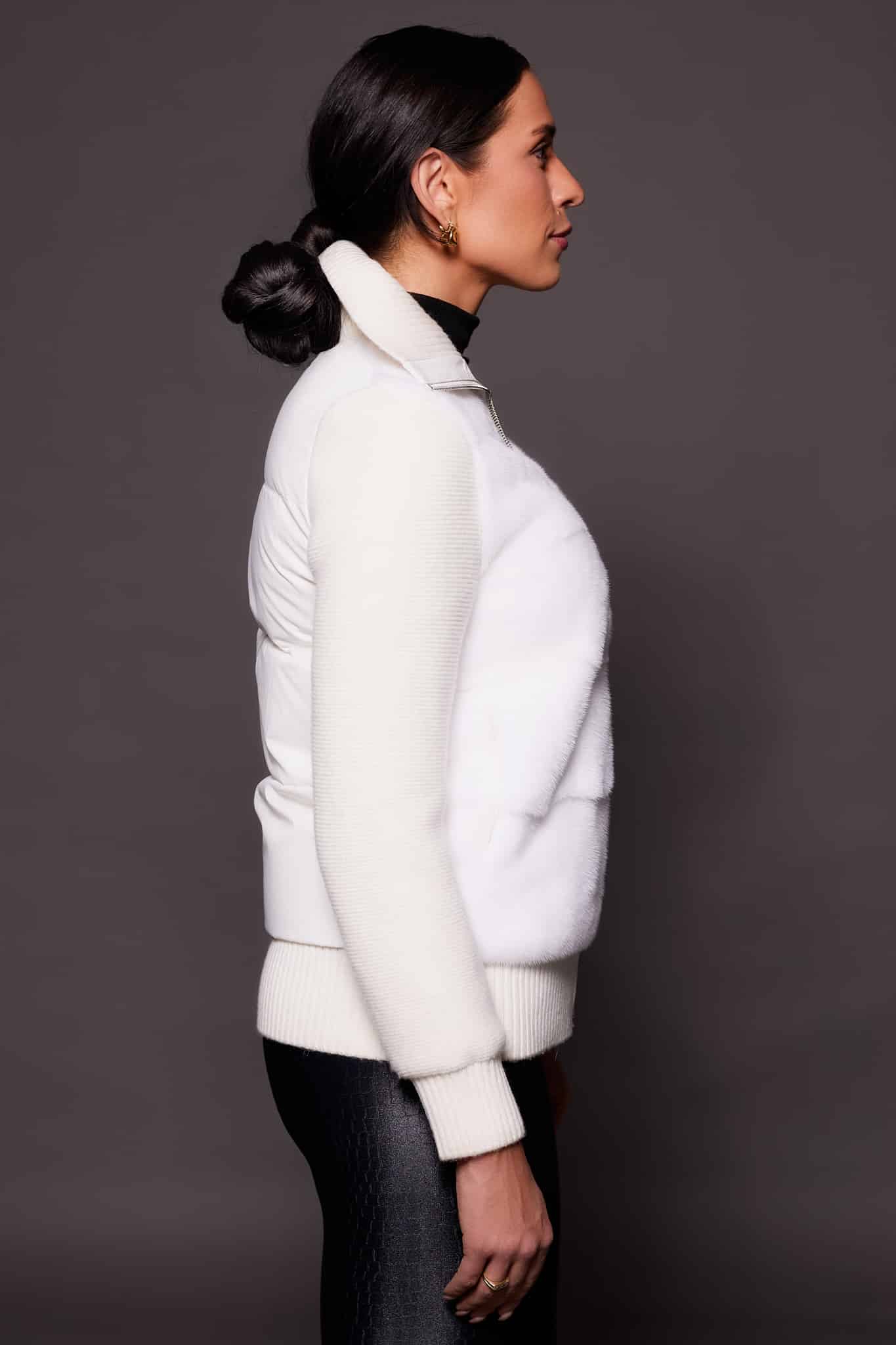 the side of a woman in a white jacket against a grey background