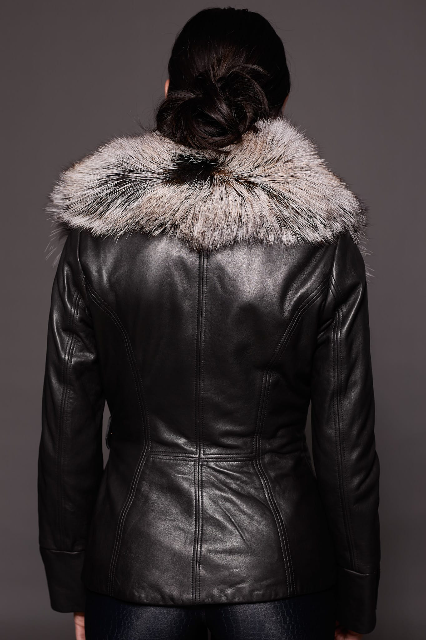the back of a woman in a black leather jacket with a brown fur trim against a dark grey background
