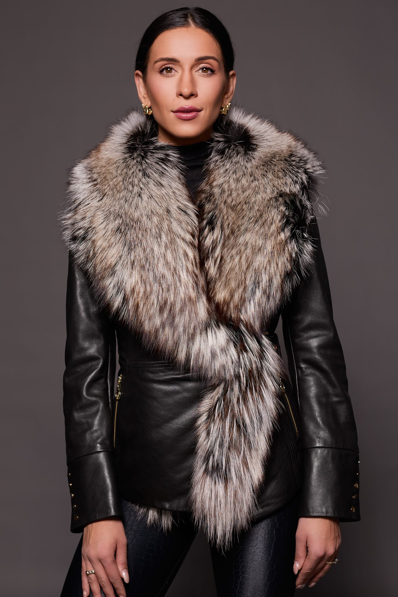 the front of a woman in a black leather jacket with a brown fur trim against a dark grey background