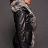 The side profile of a woman in a black leather jacket with a brown fur trim against a dark grey background