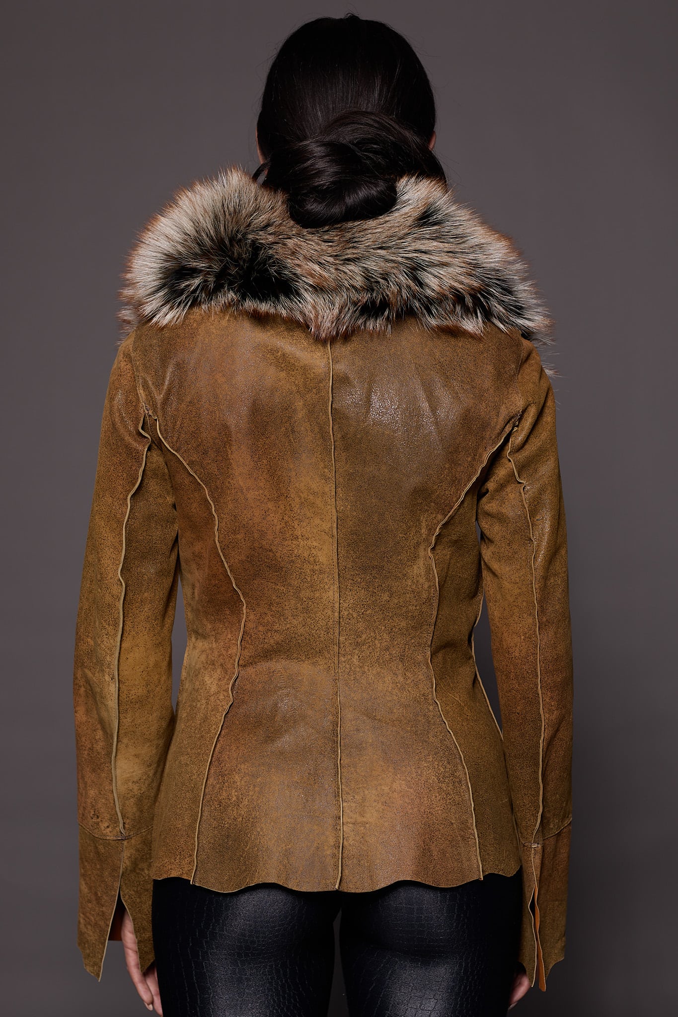 the back of a woman in a brown leather jacket with fur against a grey backdrop