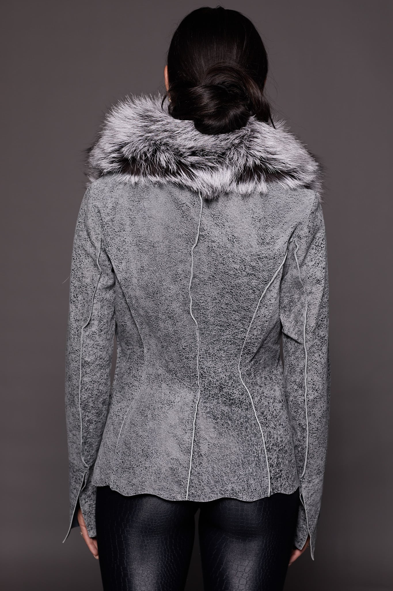 the back of a woman in a grey leather jacket with fur against a grey backdrop