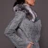 the side of a woman in a grey leather jacket with fur against a grey backdrop